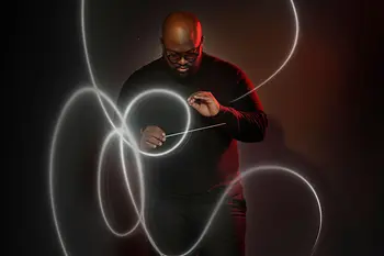 Ein Dirigent zeichnet mit den Bewegungen des Taktstocks Lichtlinien in die dunkle Umgebung.